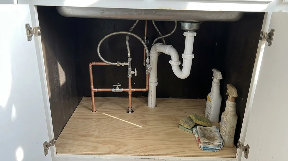 After: The same under-sink cabinet, now with new braided chrome supply lines, new shutoff valves and a clean dry cabinet floor, no bucket, same angle and same light