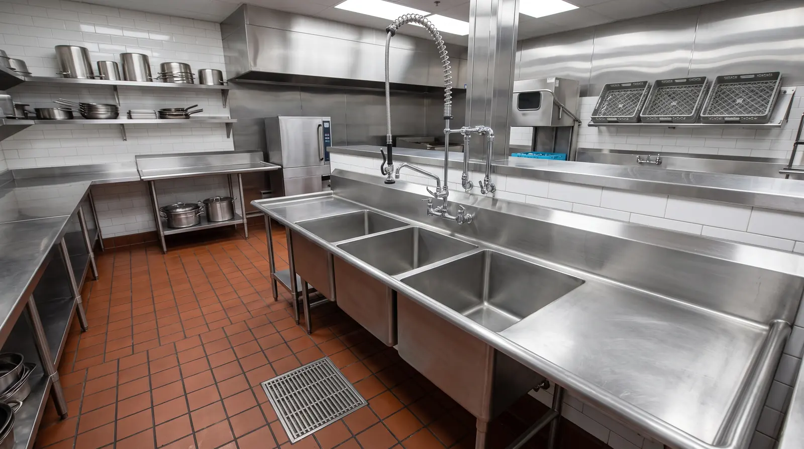 Restaurant Plumbing | Prodigy Plumbing & Drain A spotless restaurant kitchen with a three-compartment stainless steel sink, a commercial pre-rinse faucet and floor drains