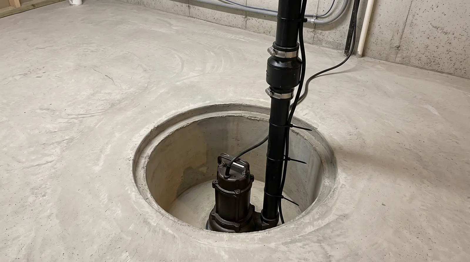 A new sump pump in a clean basement sump pit with a black discharge pipe, check valve and tidy concrete floor